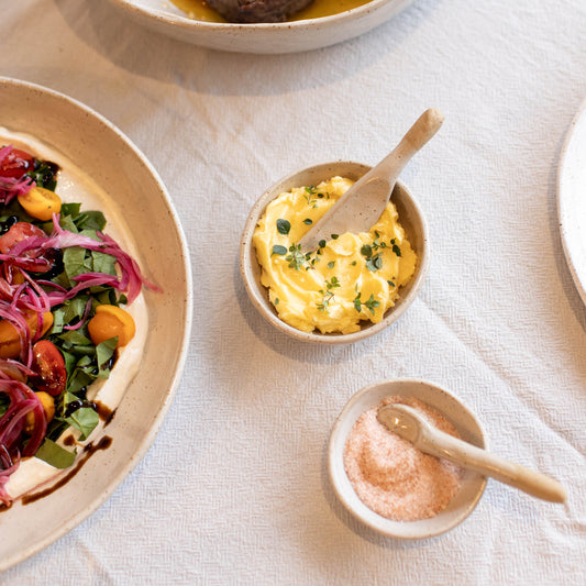 Dinner table with plates of food and small bowls of condiments on a white tablecloth.