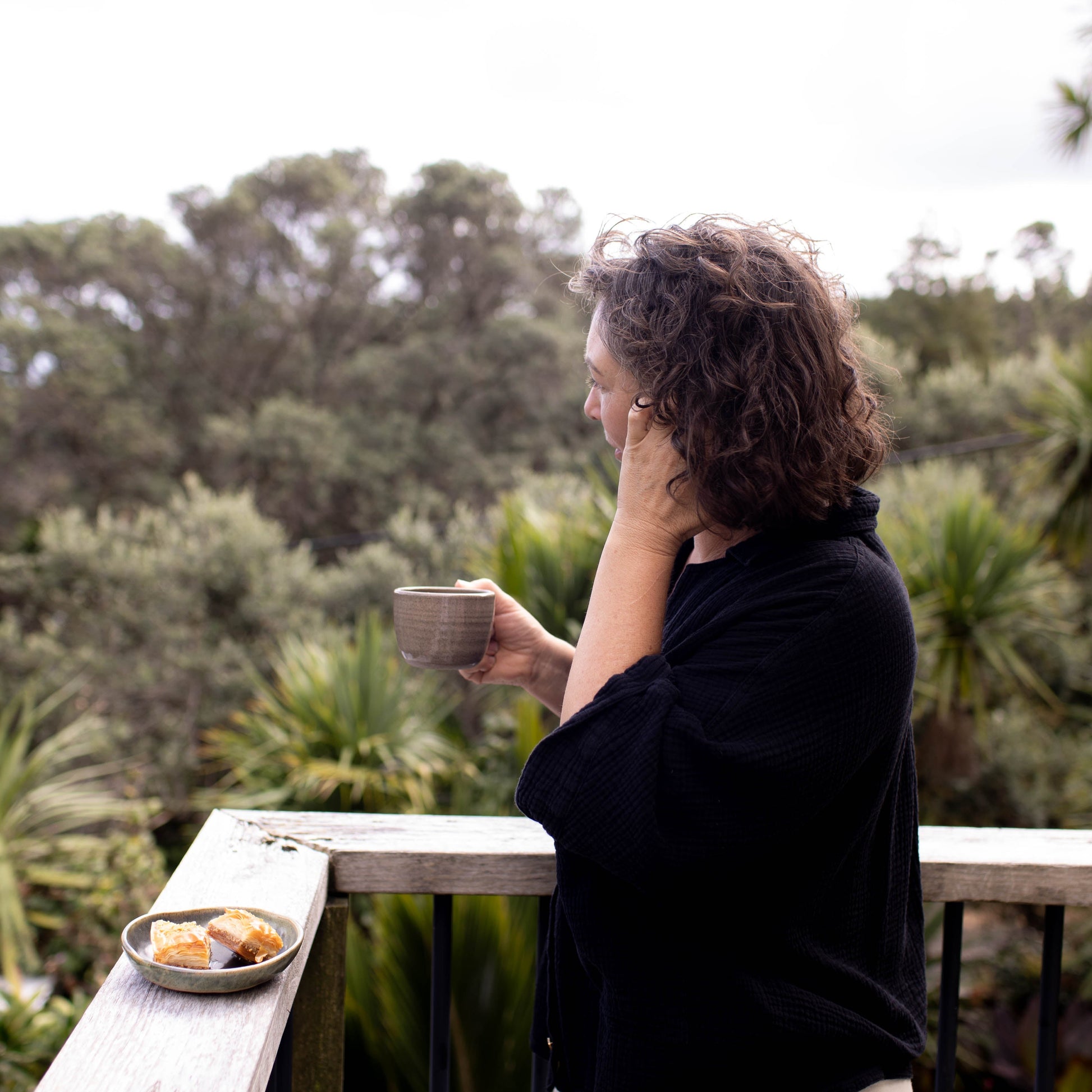 Person holding a mug on a balcony with greenery in the background