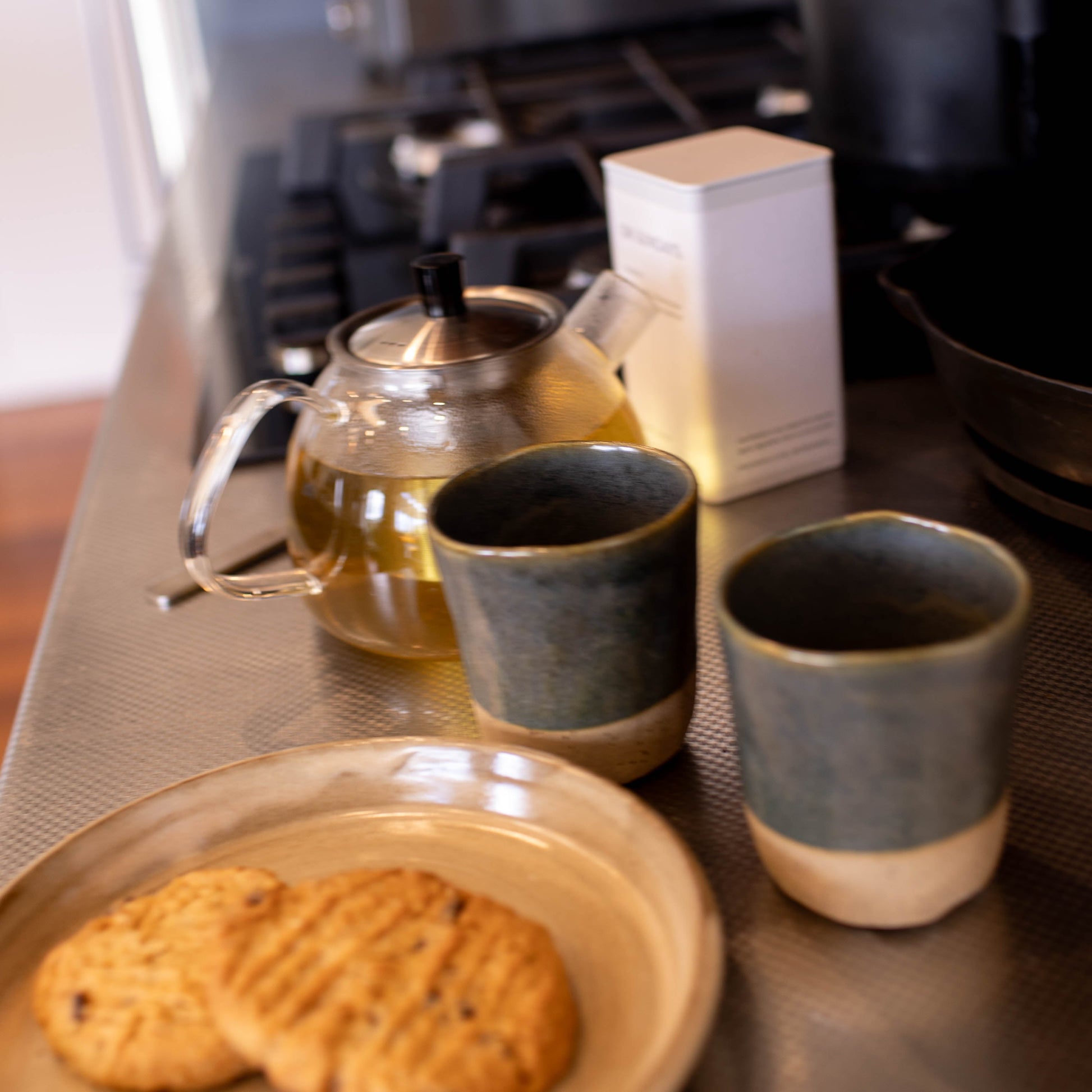 Tea set with teapot, cups, and cookies on a kitchen counter.