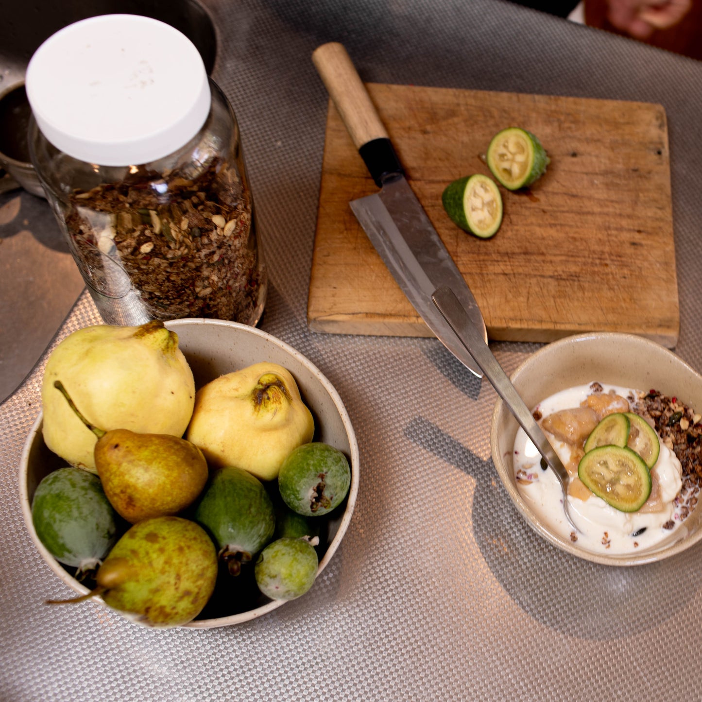 Table setting with bowls of fruit, a cutting board with sliced pears, and a jar of spices.