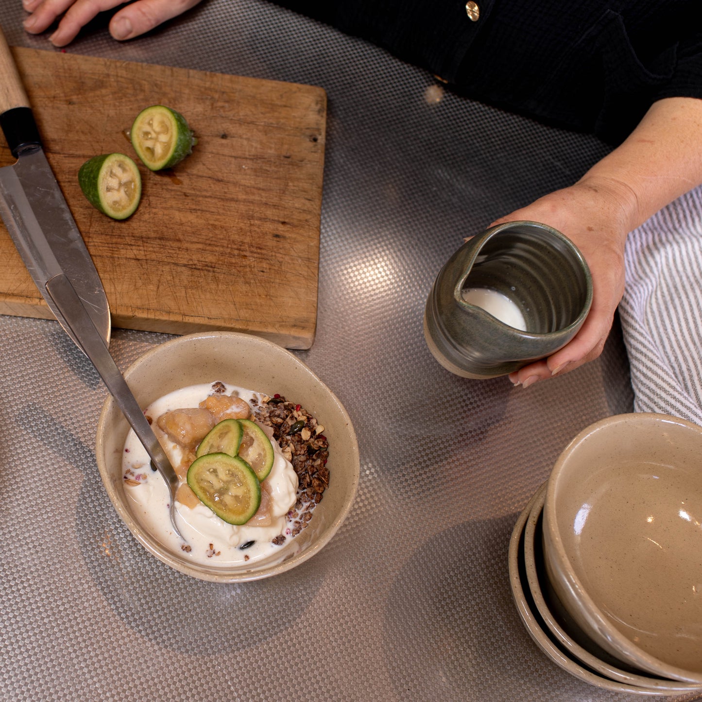 Person preparing a dish with pears and a bowl of yogurt on a kitchen counter.