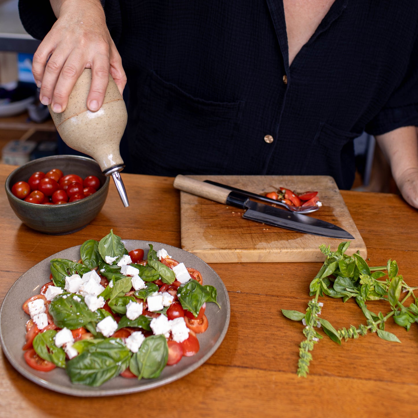 Woman pouring dressing over a salad on a wooden table