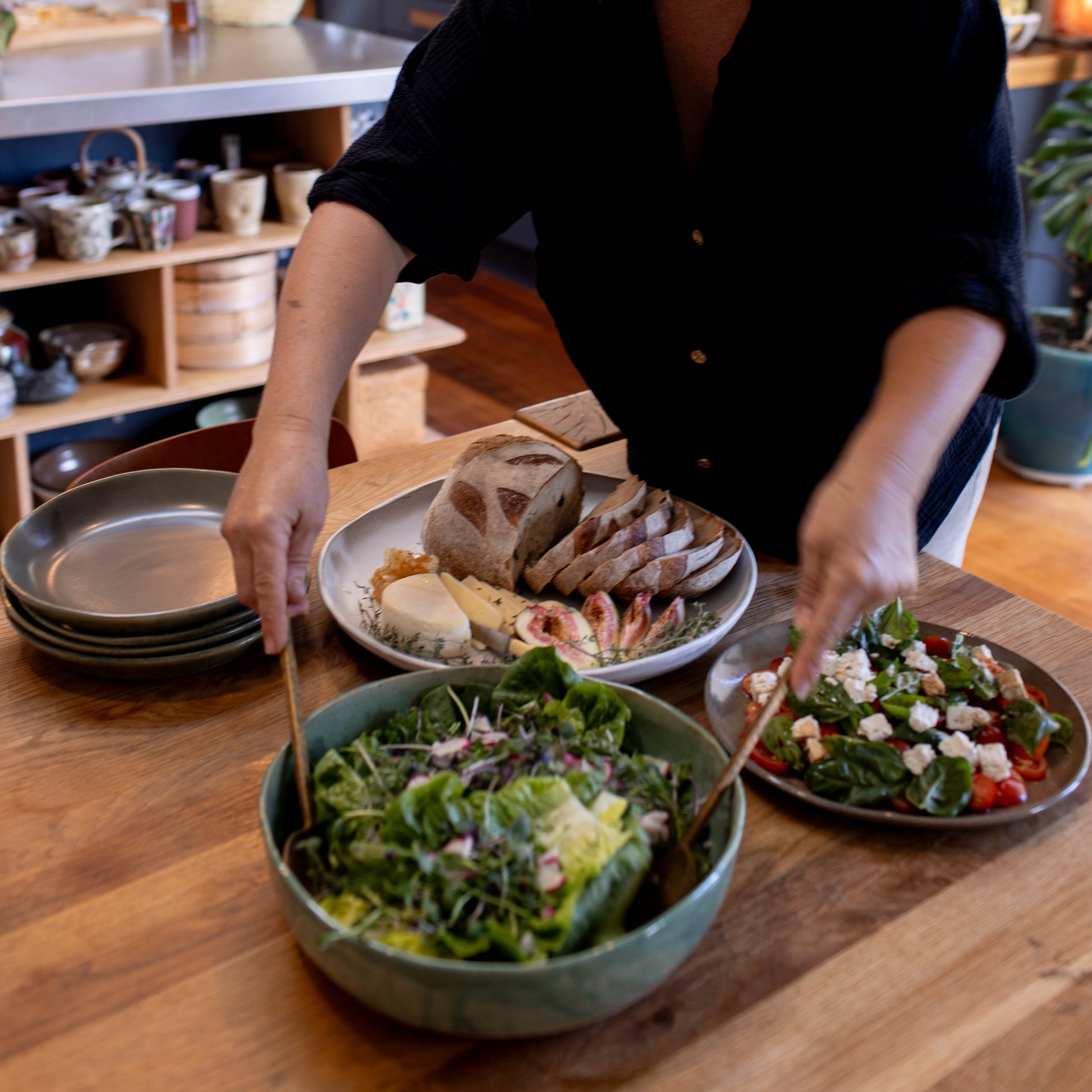 Lily preparing a meal with salad in our Lil Ceramics large serving bowl and bread on a wooden table in a kitchen.