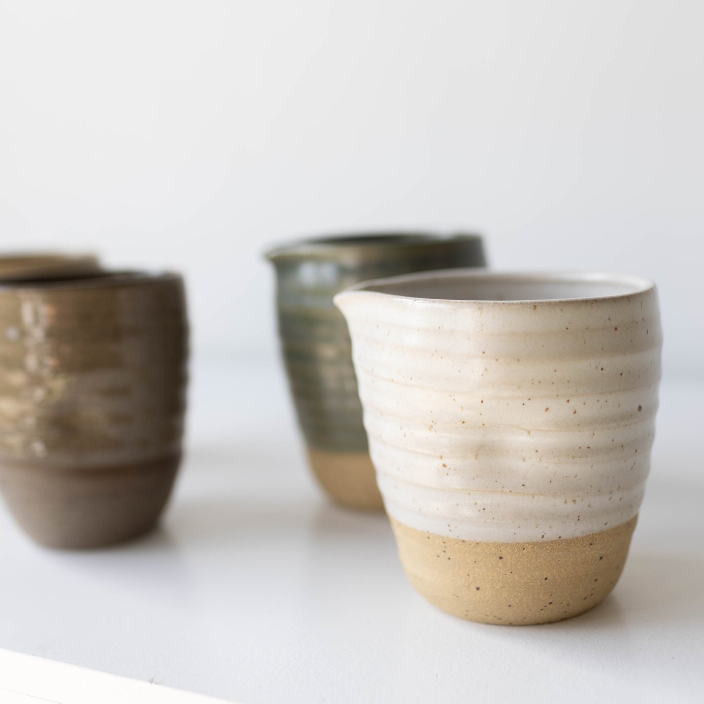 Three ceramic jugs with different glaze colours on a white surface