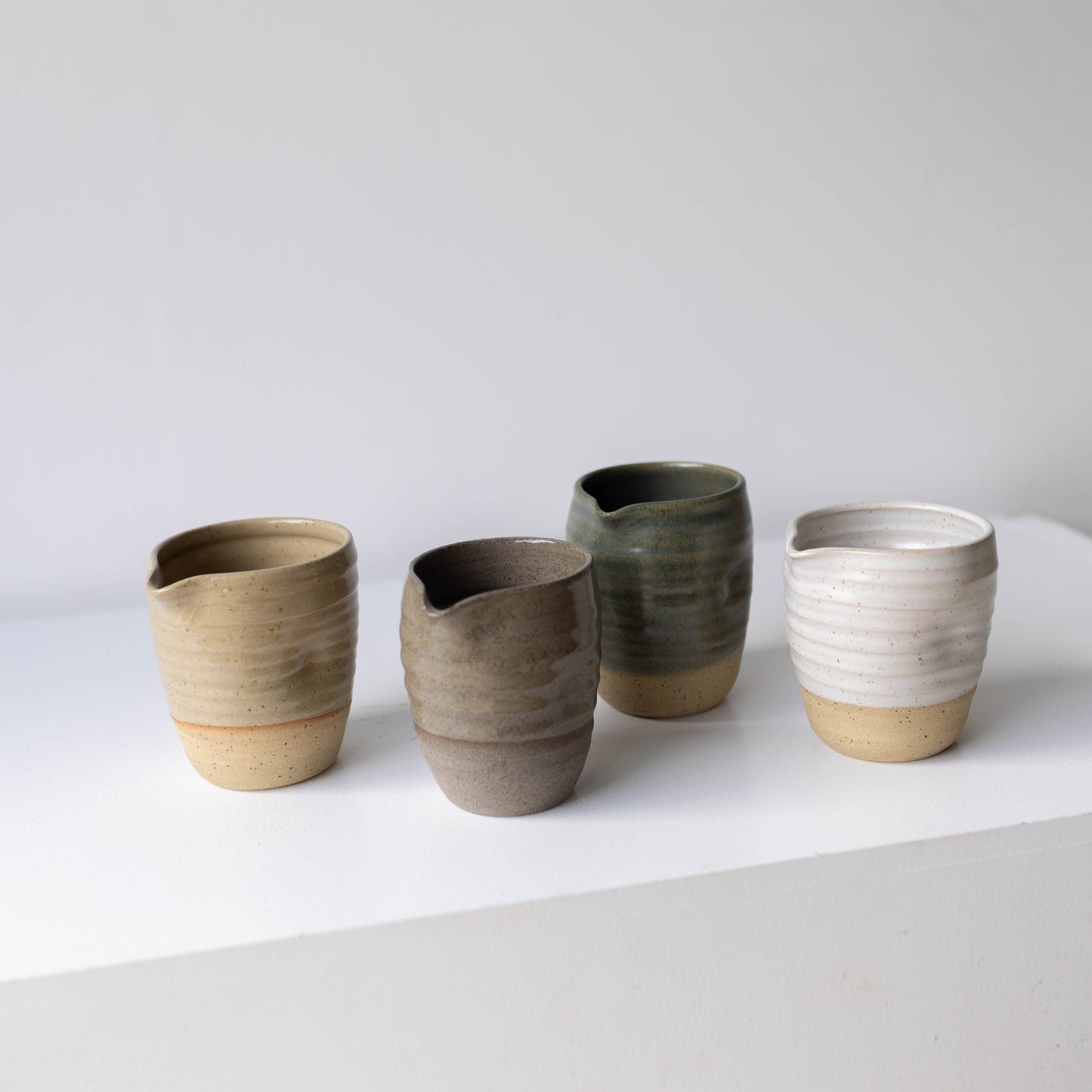 Set of four ceramic jugs with different glaze colours on a white surface and light gray background