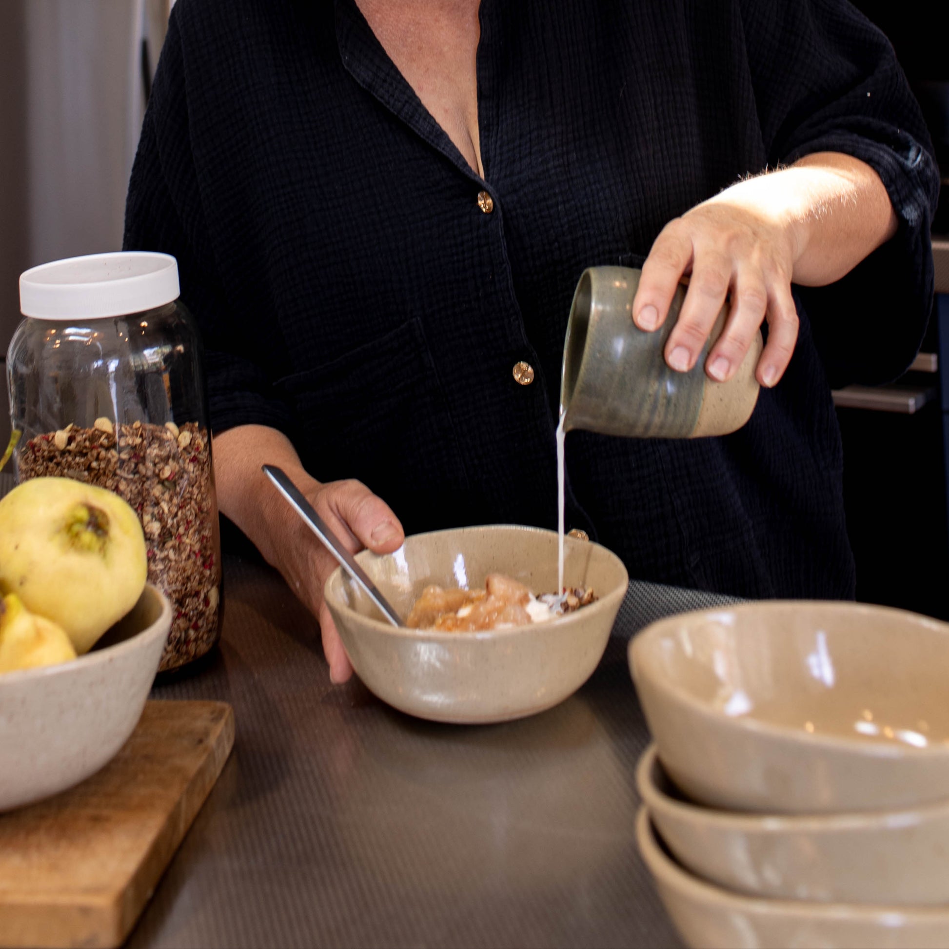Woman in a kitchen preparing food, pouring liquid from a container into a bowl.